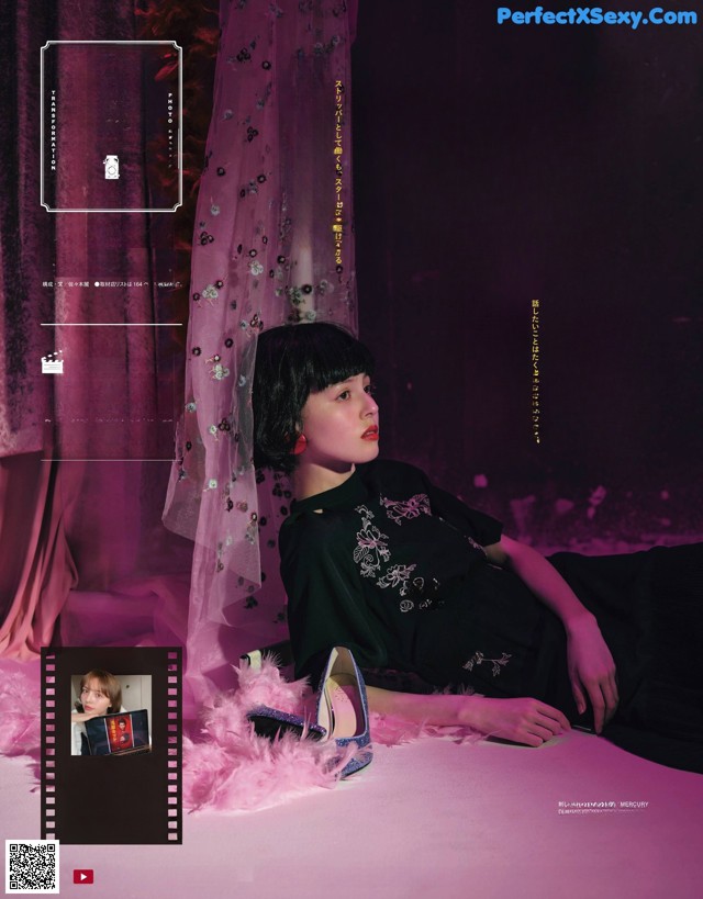 A woman in a black dress sitting on a bed.