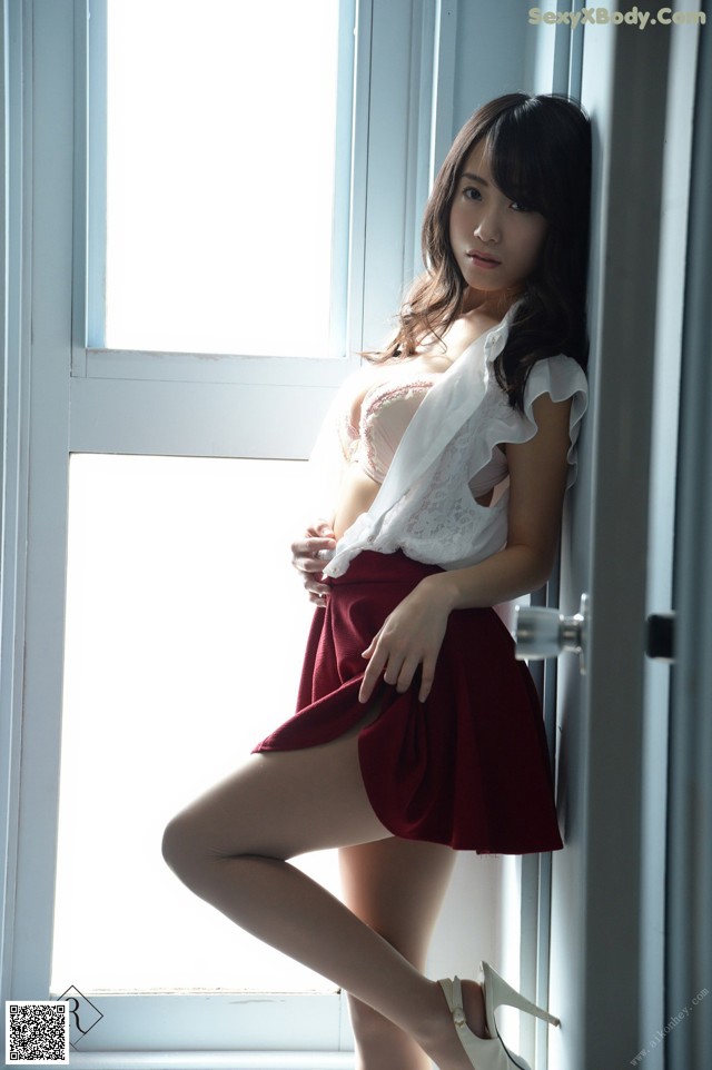 A woman in a white shirt and red skirt leaning against a window.