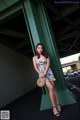 A woman in a floral dress leaning against a green pillar.