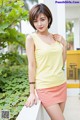 A woman in a yellow tank top and pink skirt posing for a picture.