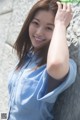 A woman leaning against a stone wall with her hand on her head.