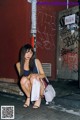 A woman sitting on the sidewalk with a white bag.