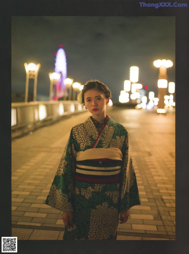 A woman in a kimono standing on a sidewalk at night.