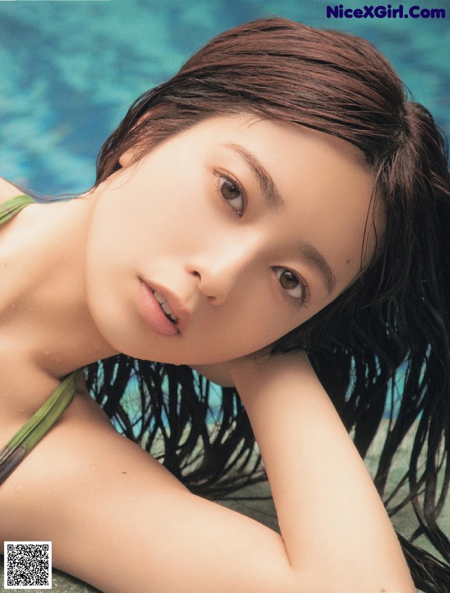 A woman in a green bikini laying on the edge of a pool.
