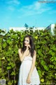 A woman in a white dress standing in front of a fence.