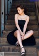 A woman in a black dress sitting on some stairs.