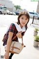 A woman in a plaid shirt carrying a brown and white bag.