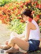 A woman sitting on the ground in front of a bush of flowers.